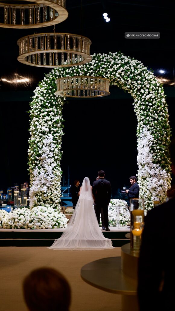 Cerimônia de João e Bárbara com arco de flores e iluminação cênica.